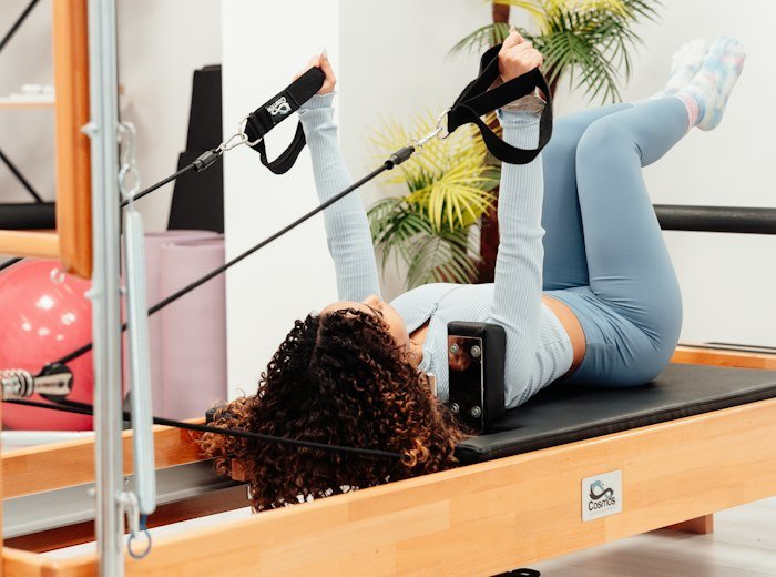 A member on her back with legs raised in the reformer straps